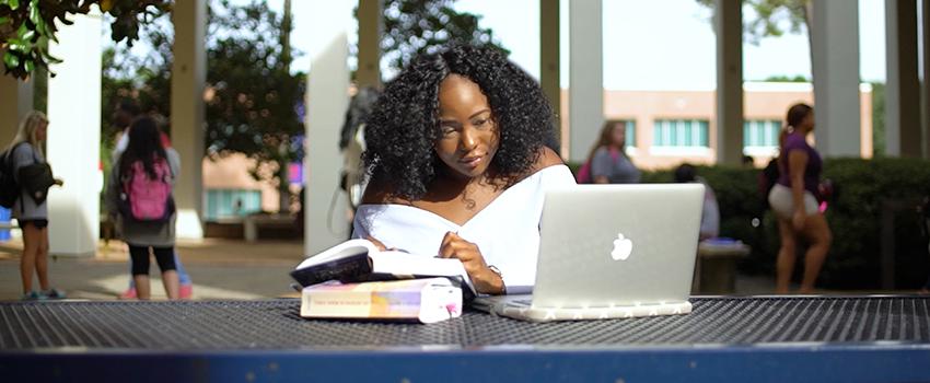 Student sitting outside of Humanities with laptop studying.